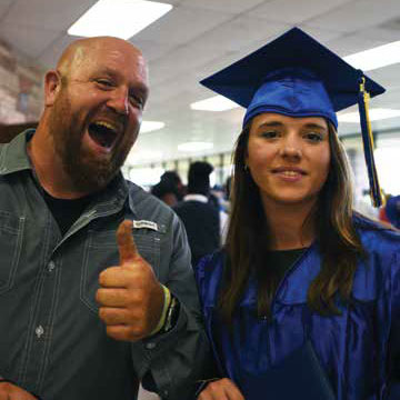 Two people smiling. One person giving the thumbs up and the other is wearing a blue graduation cap and gown